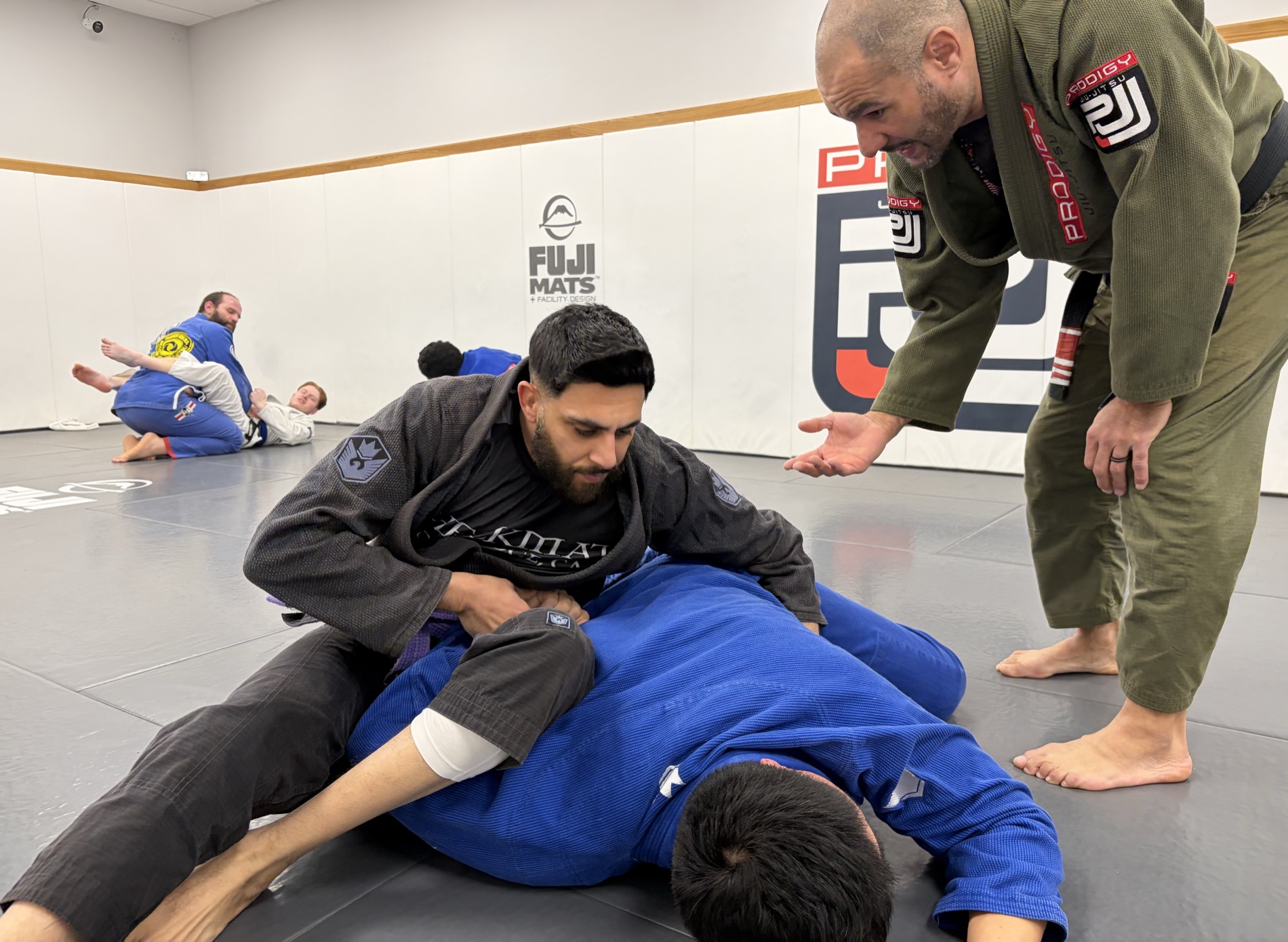 Adults rolling in the gi as a coach instructs during an adult Jiu-Jitsu class at Prodigy